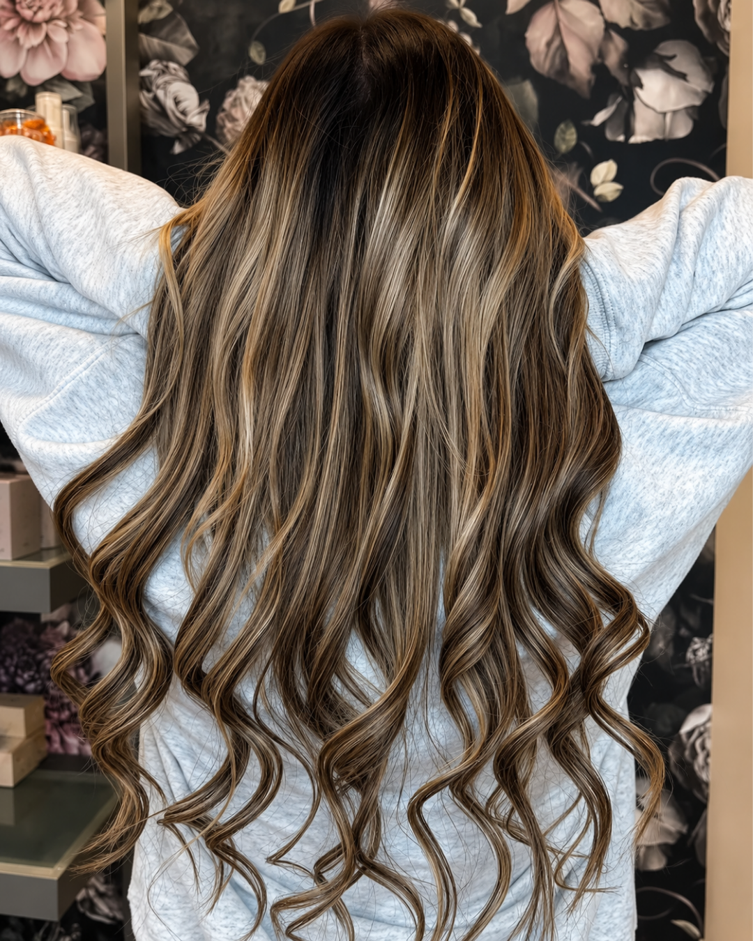 Client showing long brunette hair extensions with caramel balayage, arms raised, back view