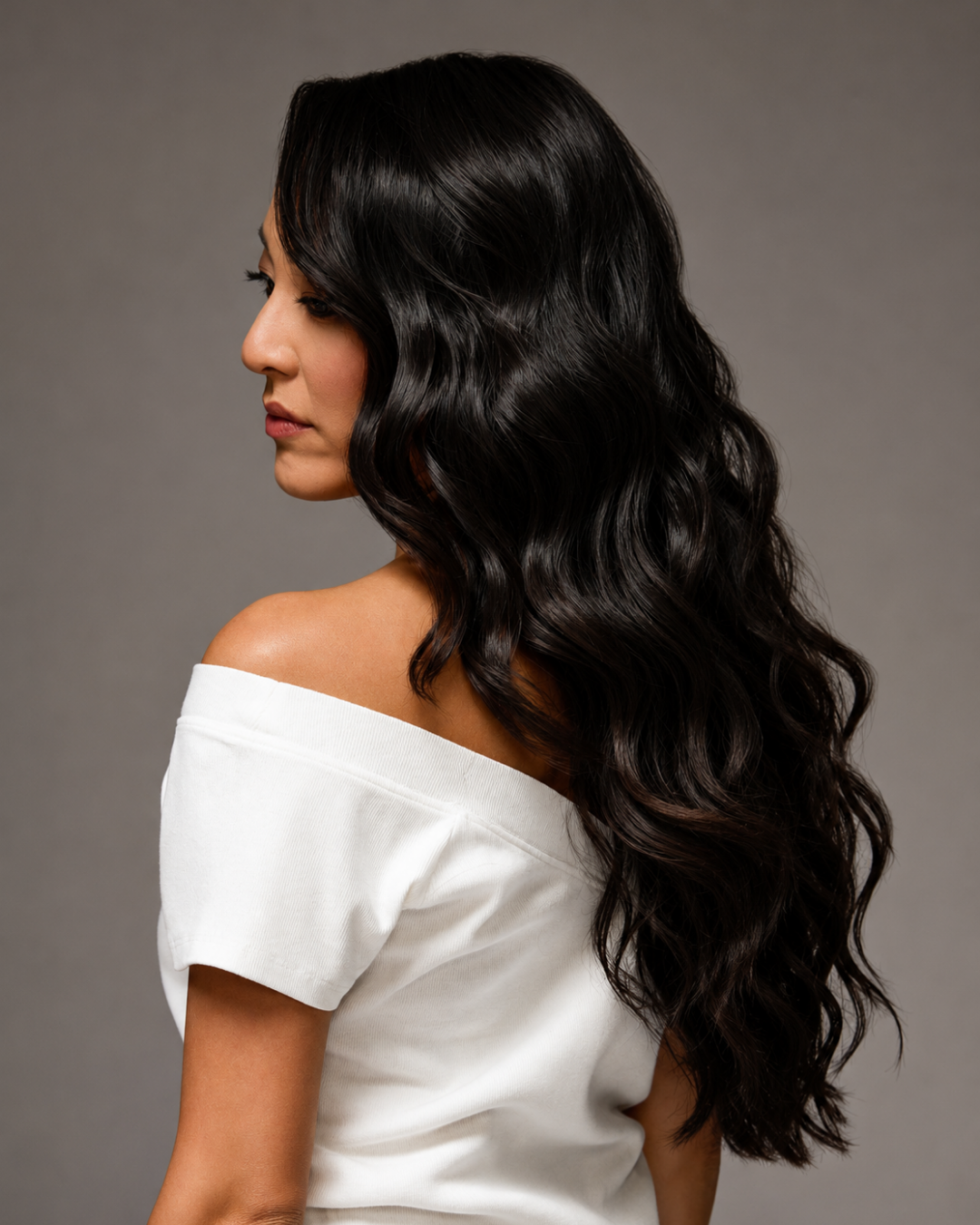 Client with long, glossy dark hair extensions styled in soft waves, studio portrait